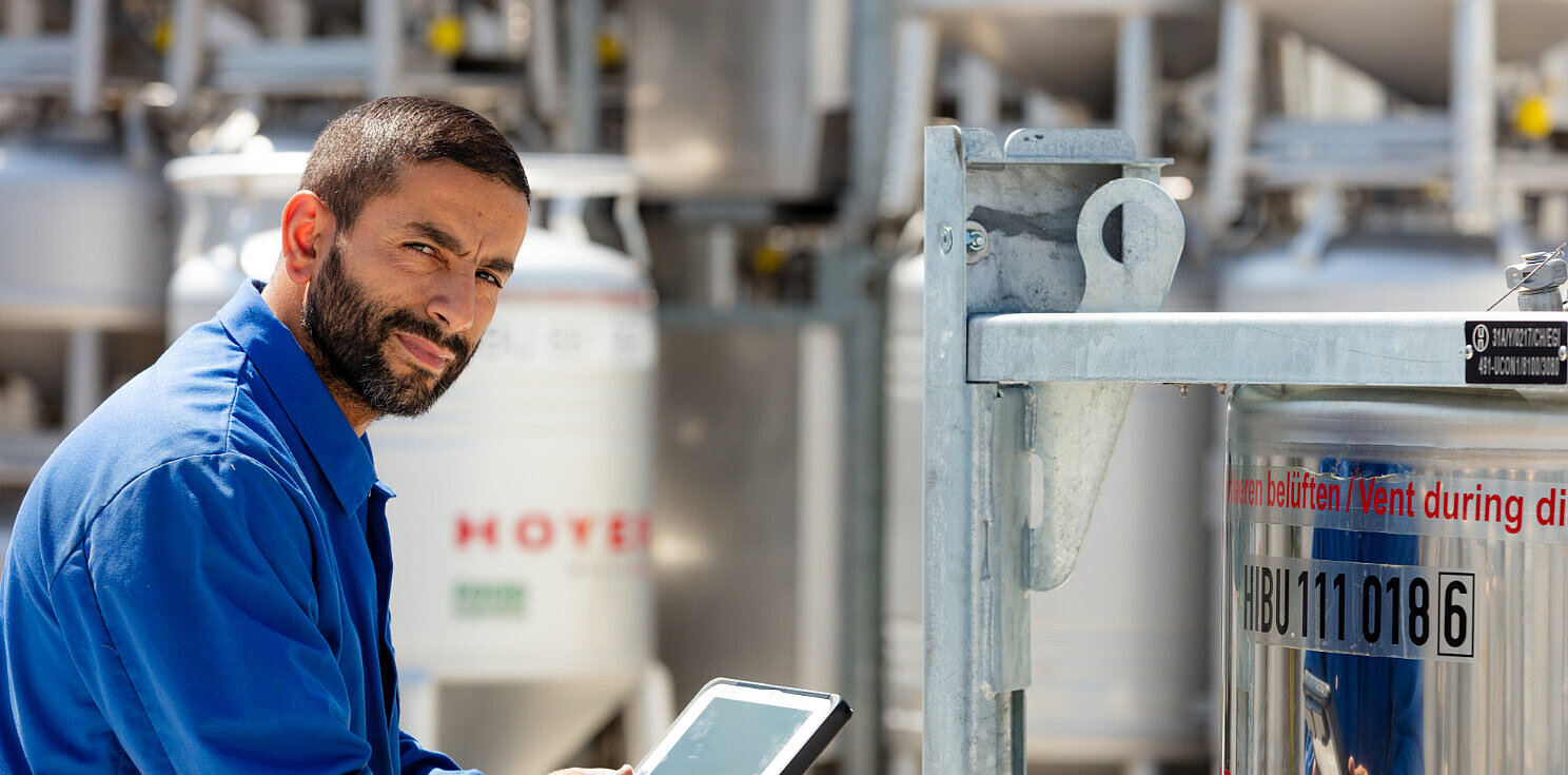 Mitarbeiter steht vor einem IBC und hält ein Tablet in der Hand