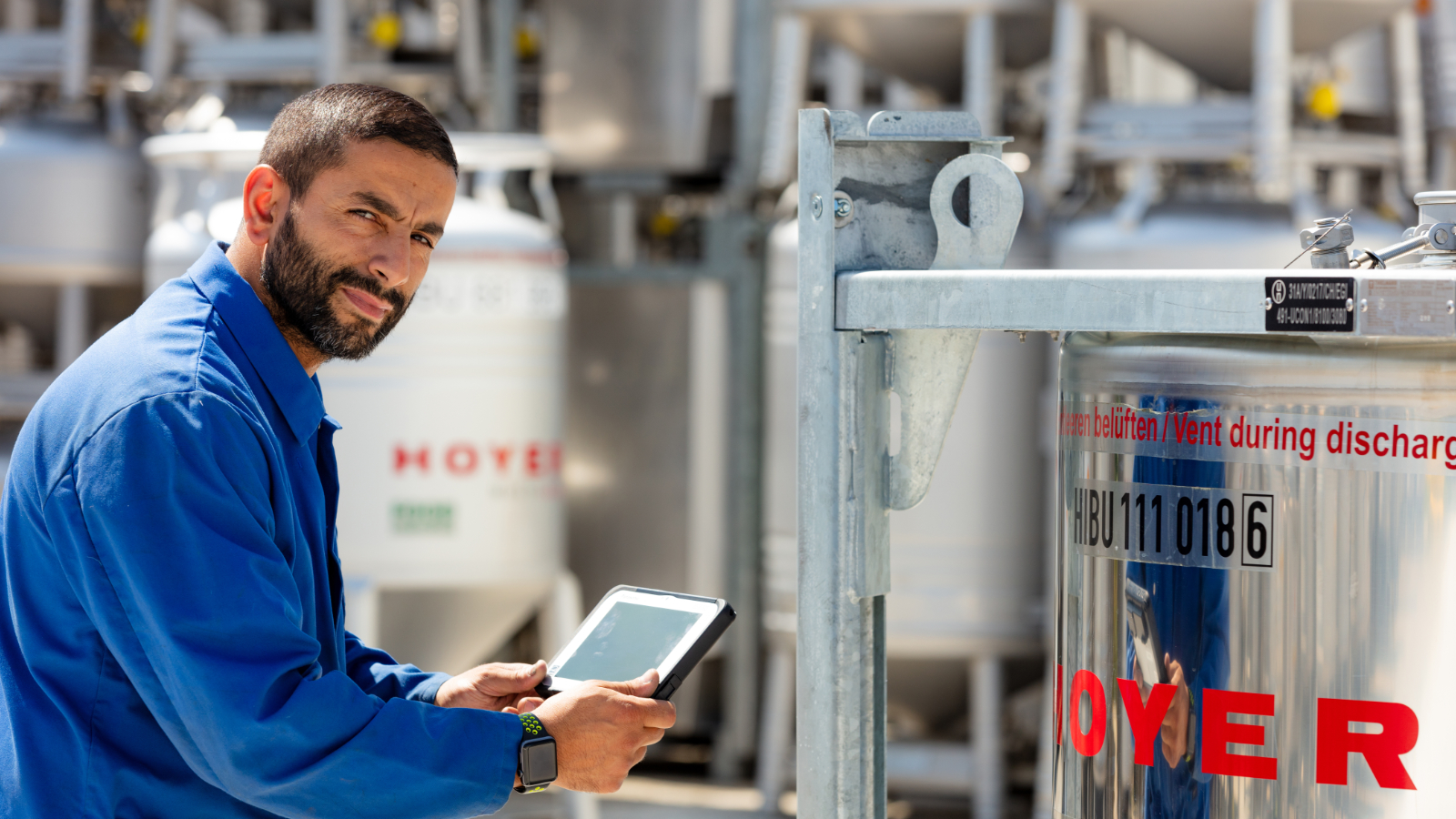 Un employé se tient devant un IBC et tient une tablette à la main.